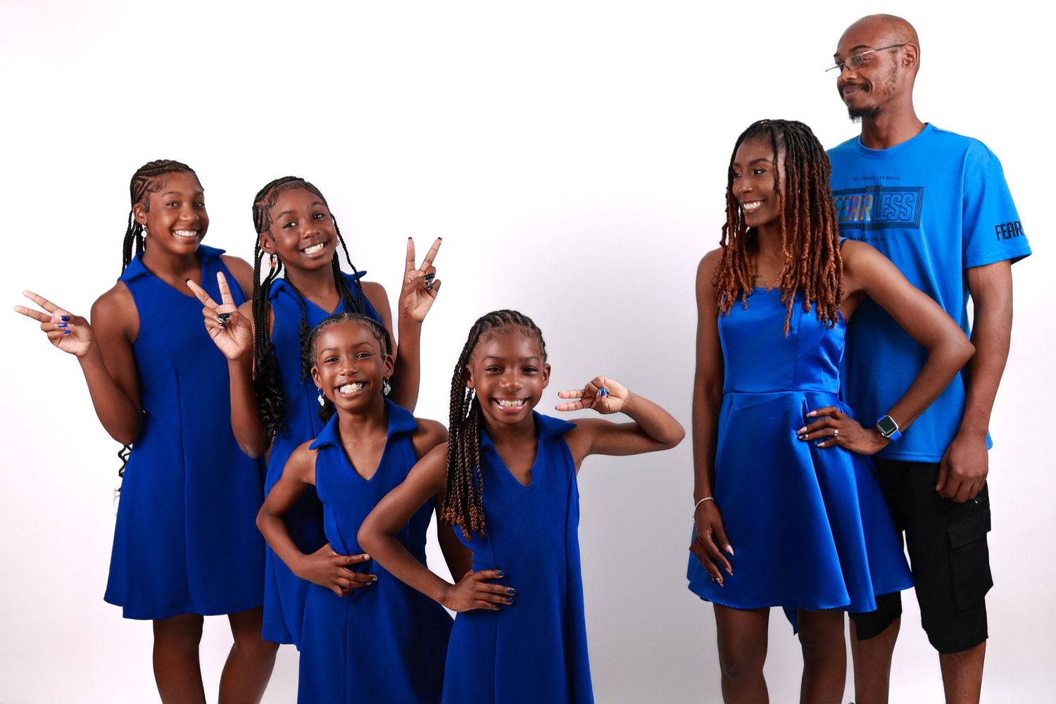 Black family of six wearing matching royal blue outfits pose playfully in a white studio setting.