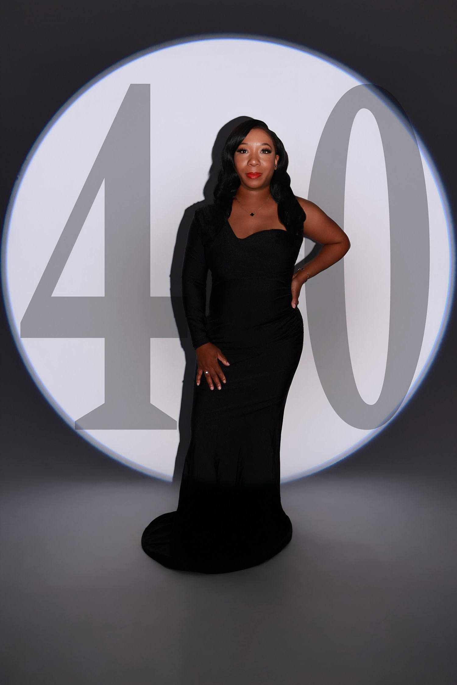 Elegant woman in black gown posing in front of illuminated 40 backdrop for milestone birthday portrait.