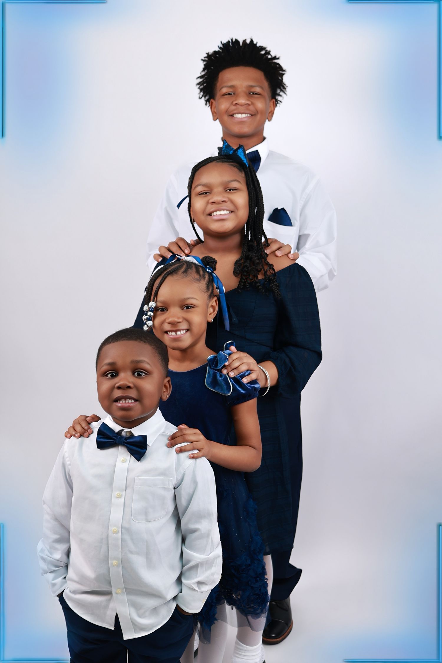 Four Black children in coordinating navy and white formal outfits pose together for a studio portrait.