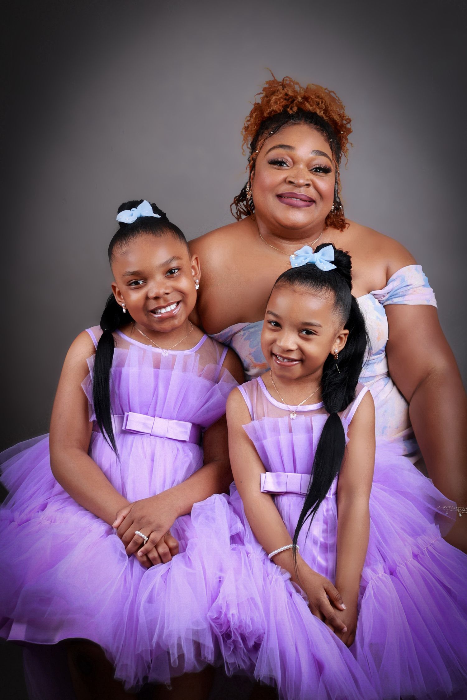 Mother and two daughters in matching purple tutu dresses pose together in studio.