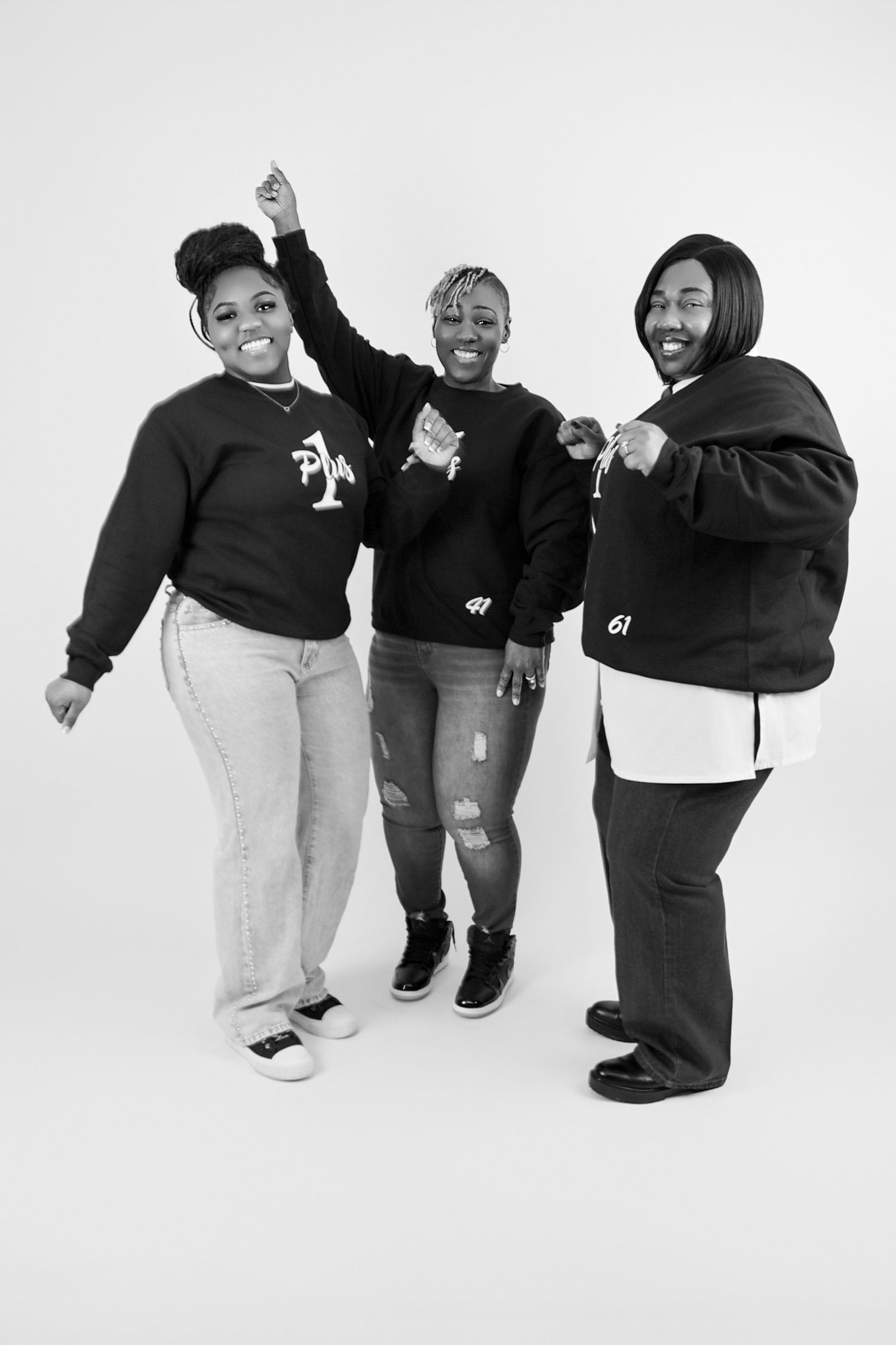 Three Black women laugh and dance together in a fun black and white studio portrait.