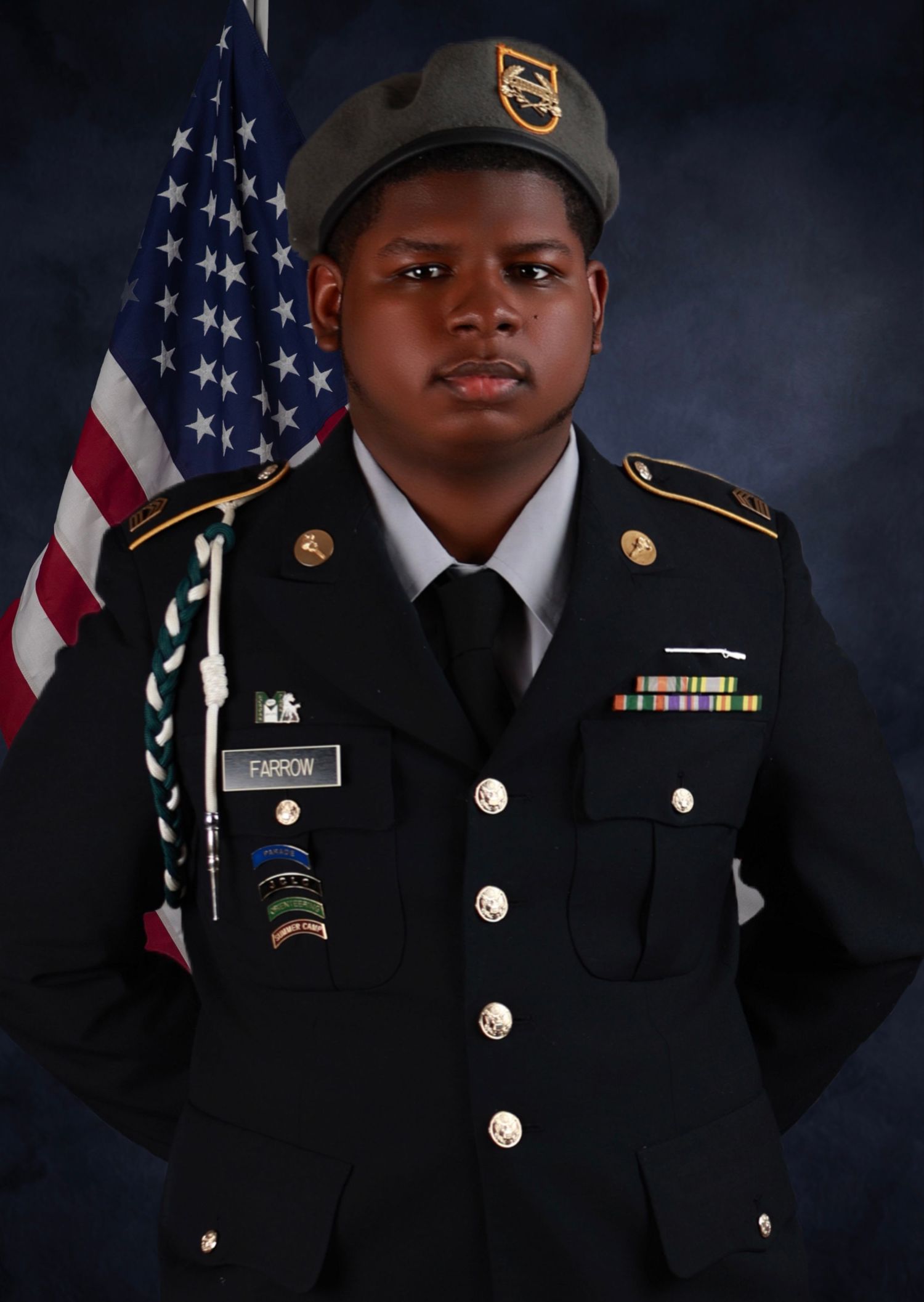 Young person in US Army dress uniform with beret and ribbons posing before American flag.