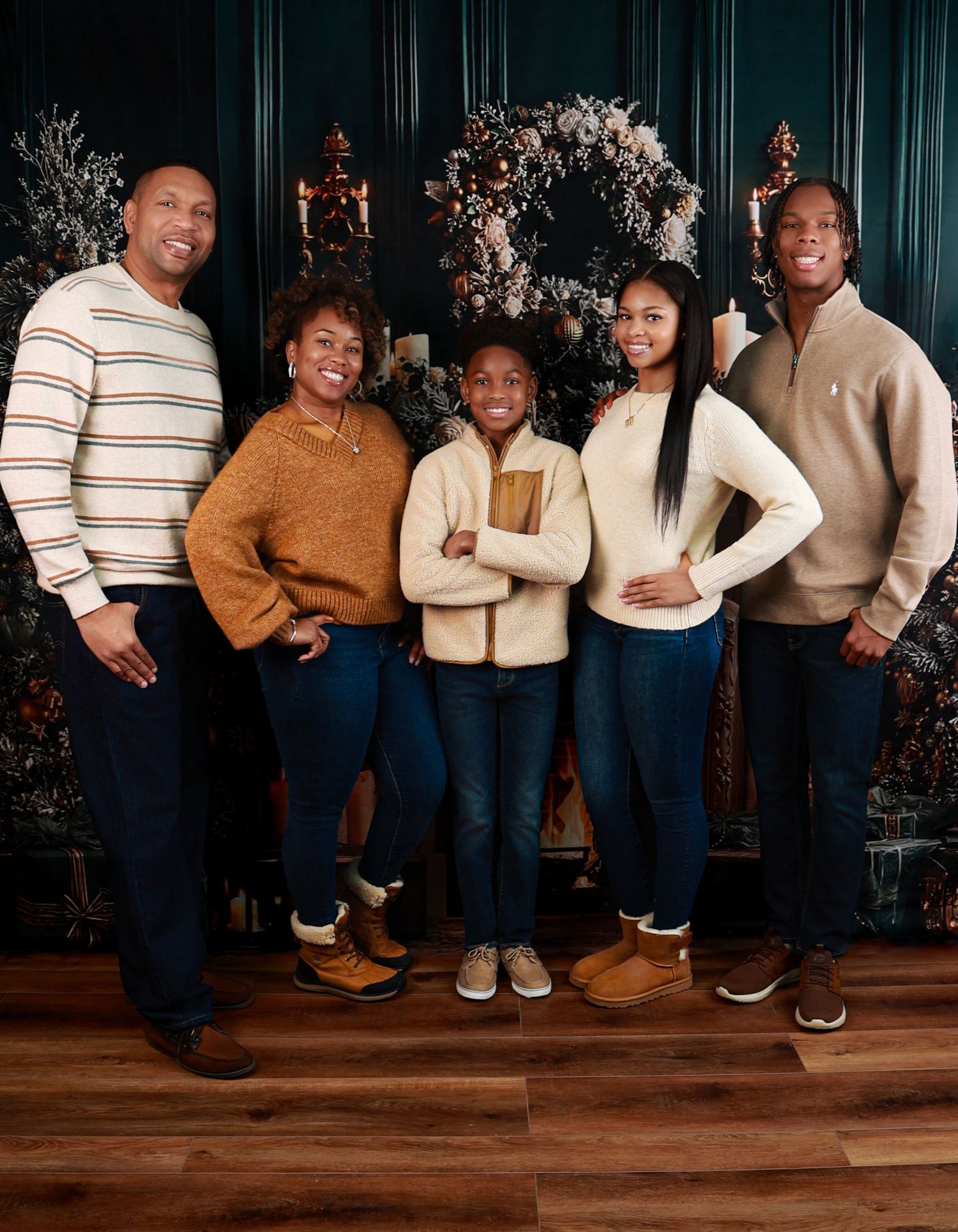 A family of five poses warmly together in casual winter attire in front of a festive holiday wreath decoration.