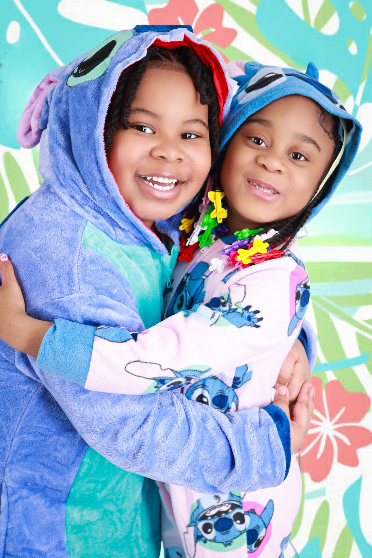 Two children hugging in Lilo and Stitch costumes on tropical background.
