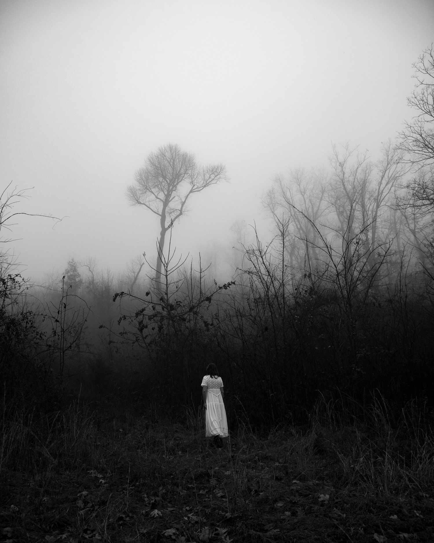 black and white image of a woman in a white gown with bare trees in the background