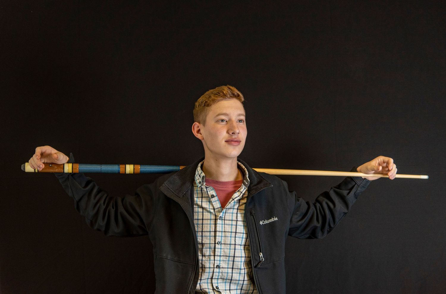young man resting his arms on pool cue across his shoulders