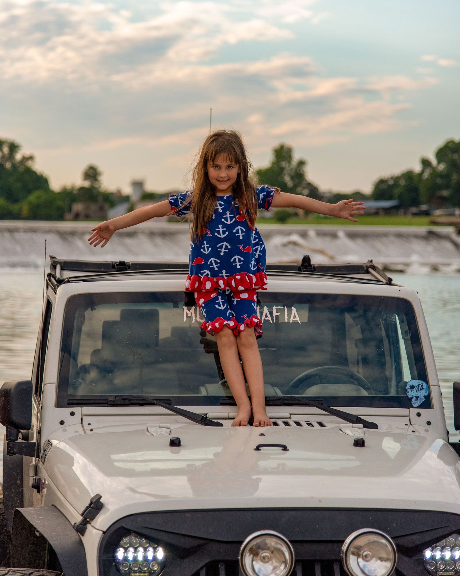 young girl standing on the hood of a white Jeep