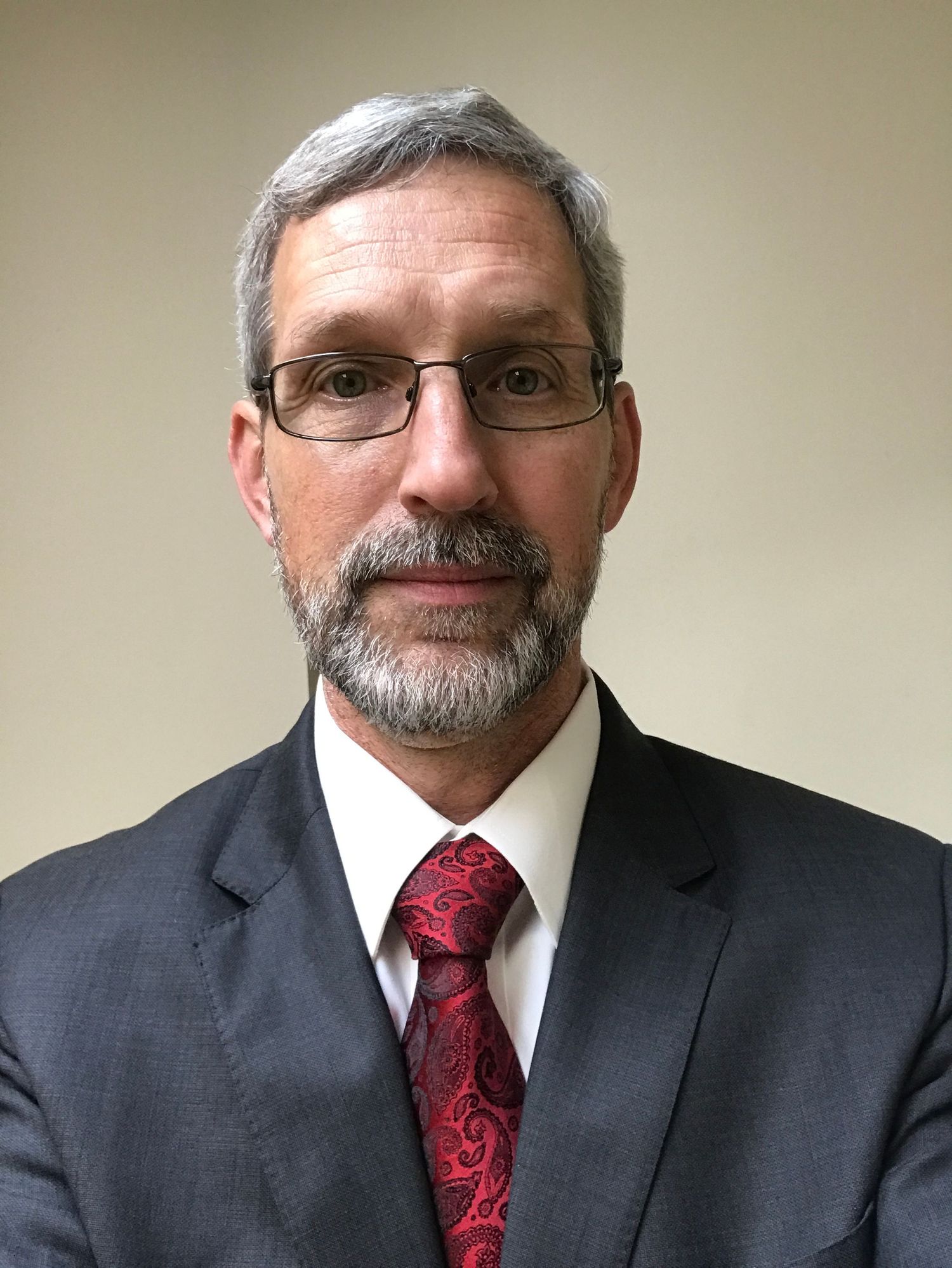 headshot of man in a dark suit with a red tie