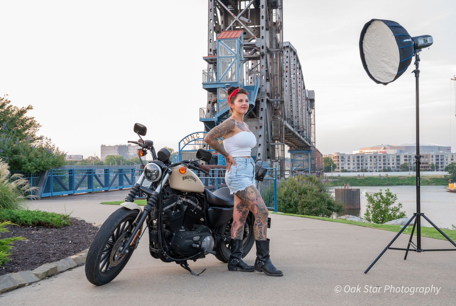 Behind-the-scenes view of a model posing with motorcycle. Lighting equipment is visible.