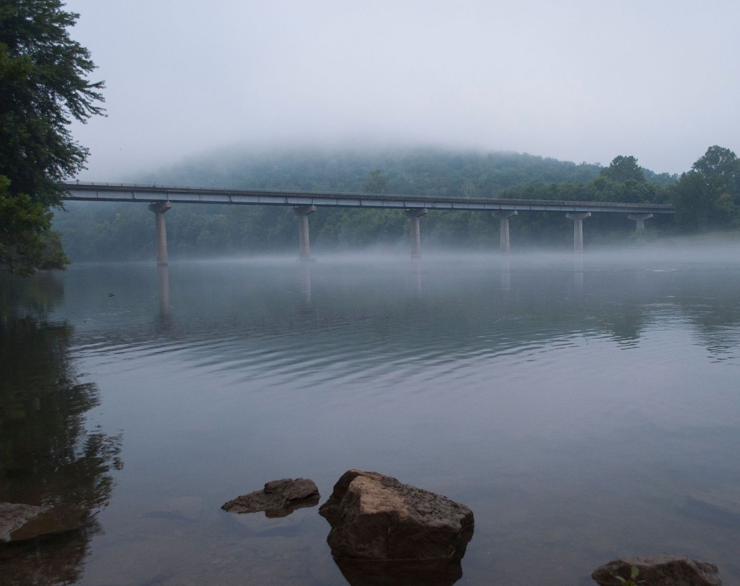 a bridge over a river with a rock in the foreground