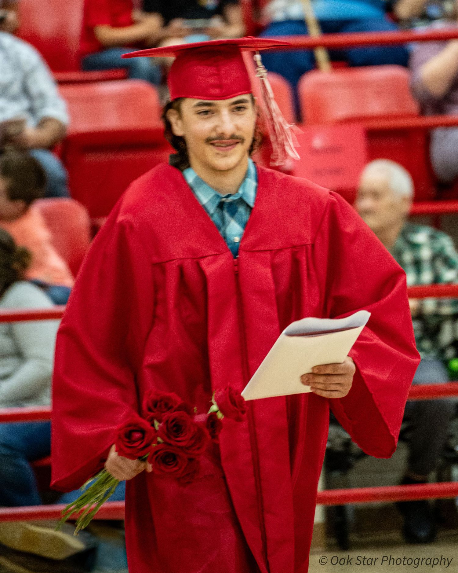Young high school graduate walking at commencement carrying diploma and roses.