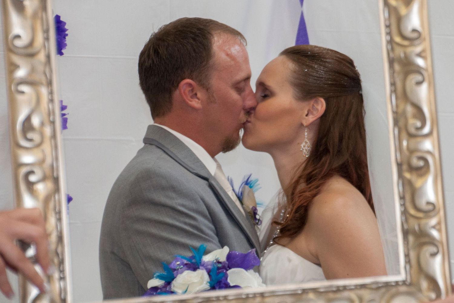 Newlywed couple kissing with an empty picture frame in the foreground.