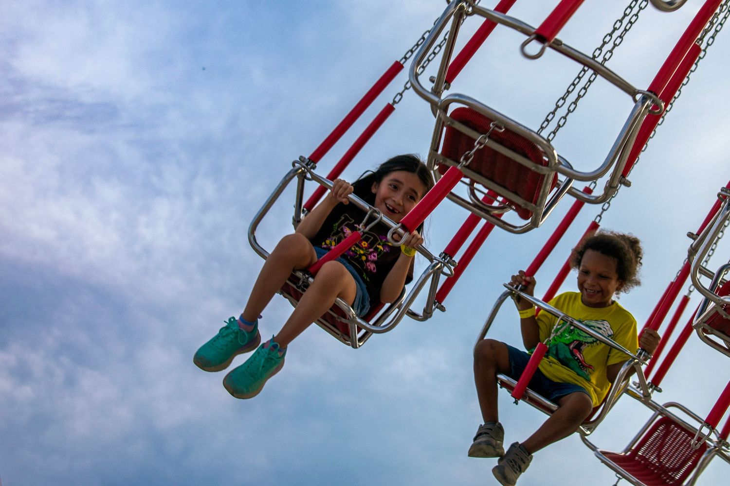 Two kids smile while enjoying a fun carnival ride at a public event. Live event photography. We capture the joy and energy of family fun