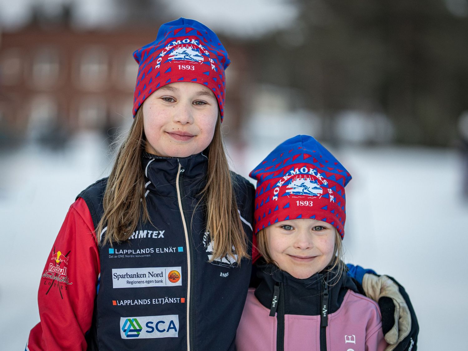 Vinterporträtt av två personer som bär matchande röda och lila vintermössor med laglogotyper.