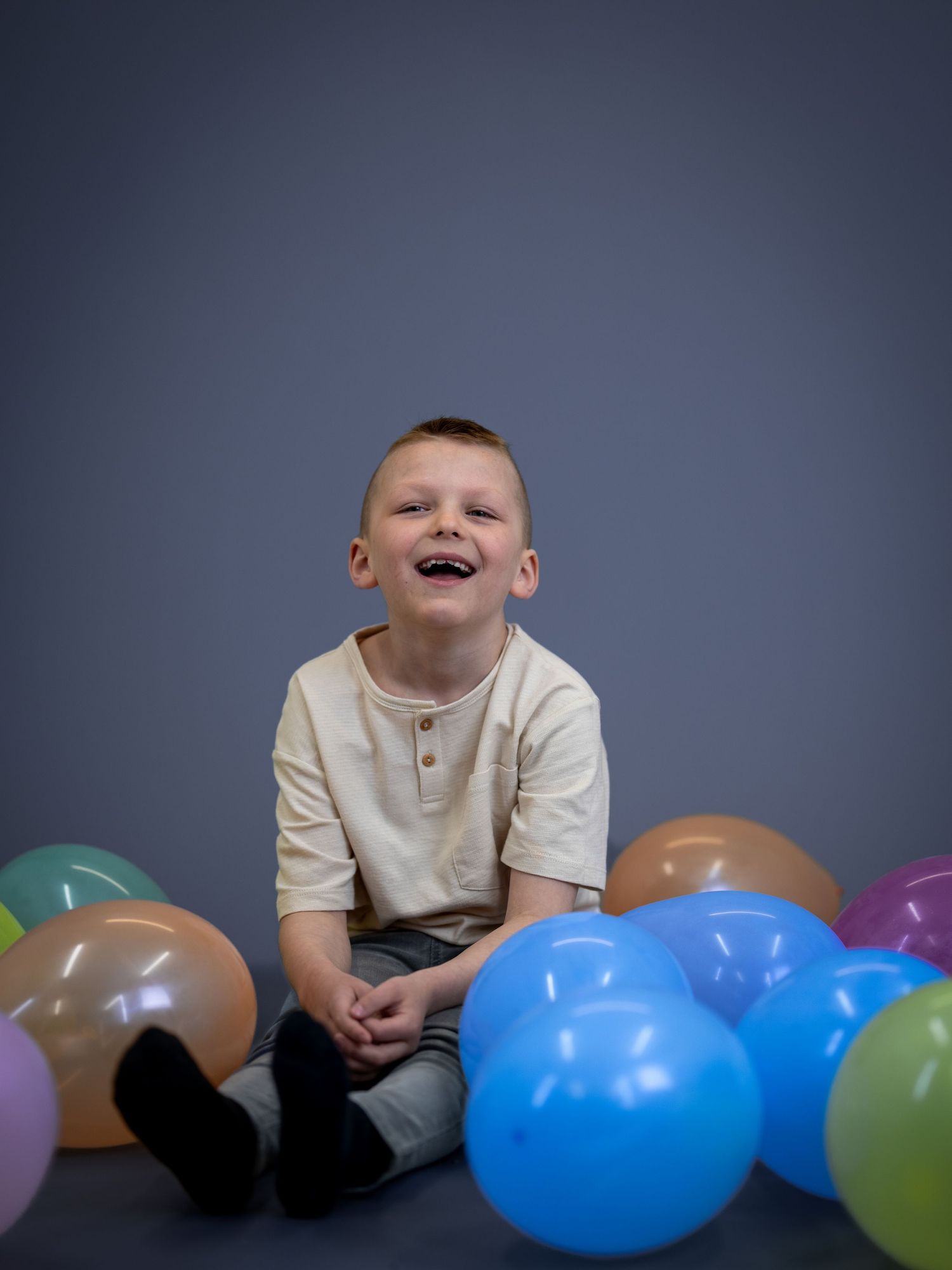 Ett litet barn sitter omgivet av färgglada ballonger mot en mörkgrå bakgrund.