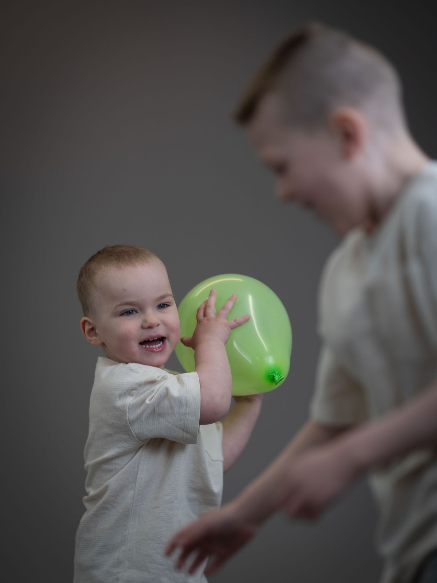 Ett glatt litet barn leker med en grön ballong medan någon tittar på i en studiomiljö.