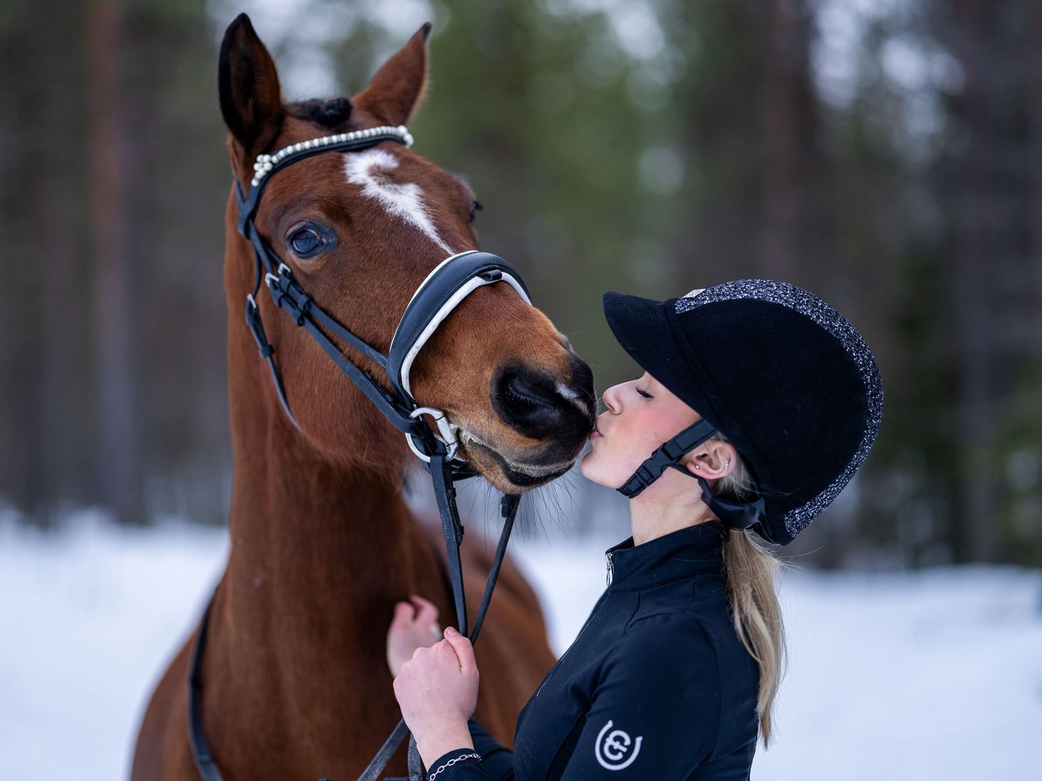 Närbild på person som justerar hästens träns under vintern med snö i bakgrunden.