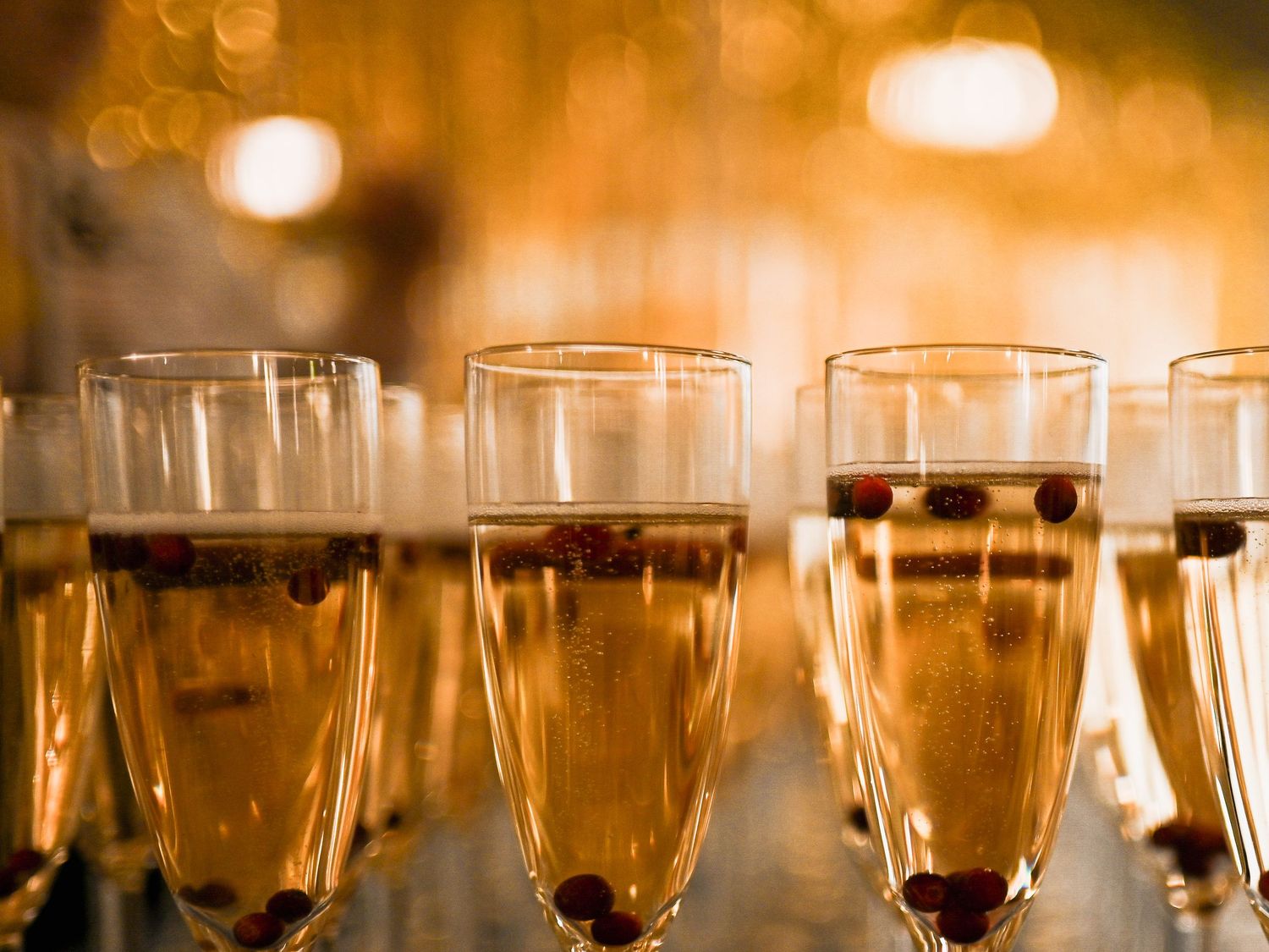 Champagneflöjter fyllda med bubblig dryck och garnering mot en varm bokeh-bakgrund.