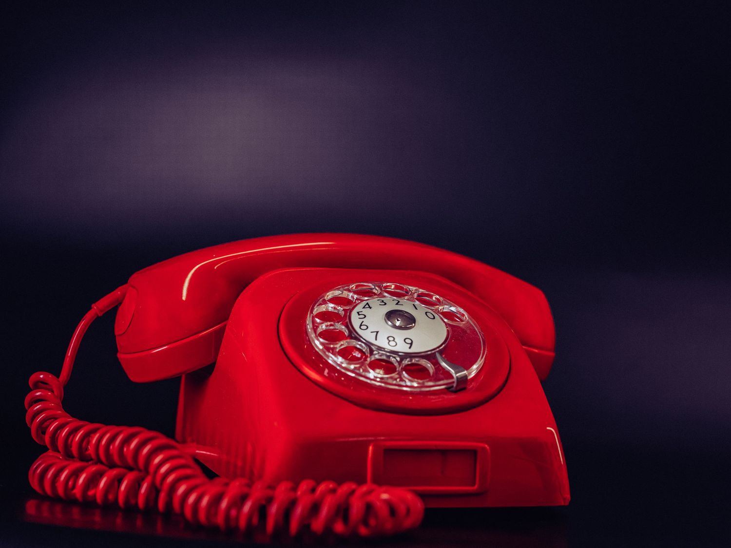 Vintage röd roterande telefon fotograferad mot mörklila bakgrund.
