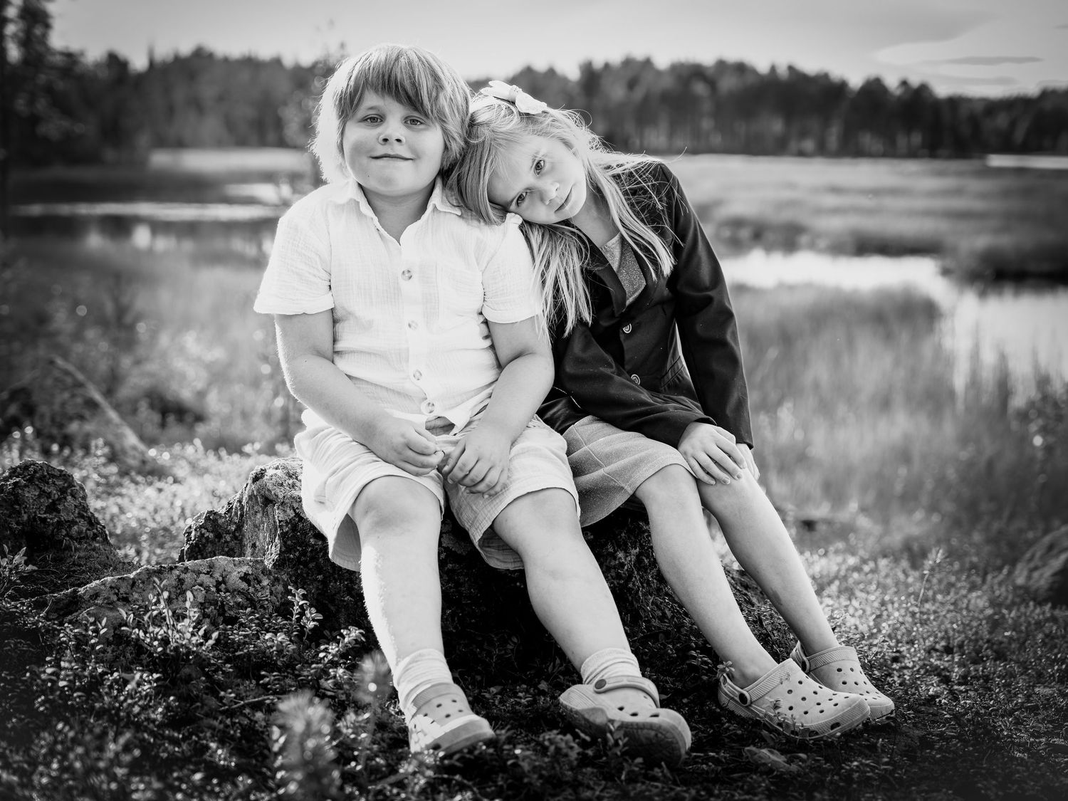 Black and white photo of people sitting together in a grassy meadow near a lake at sunset.