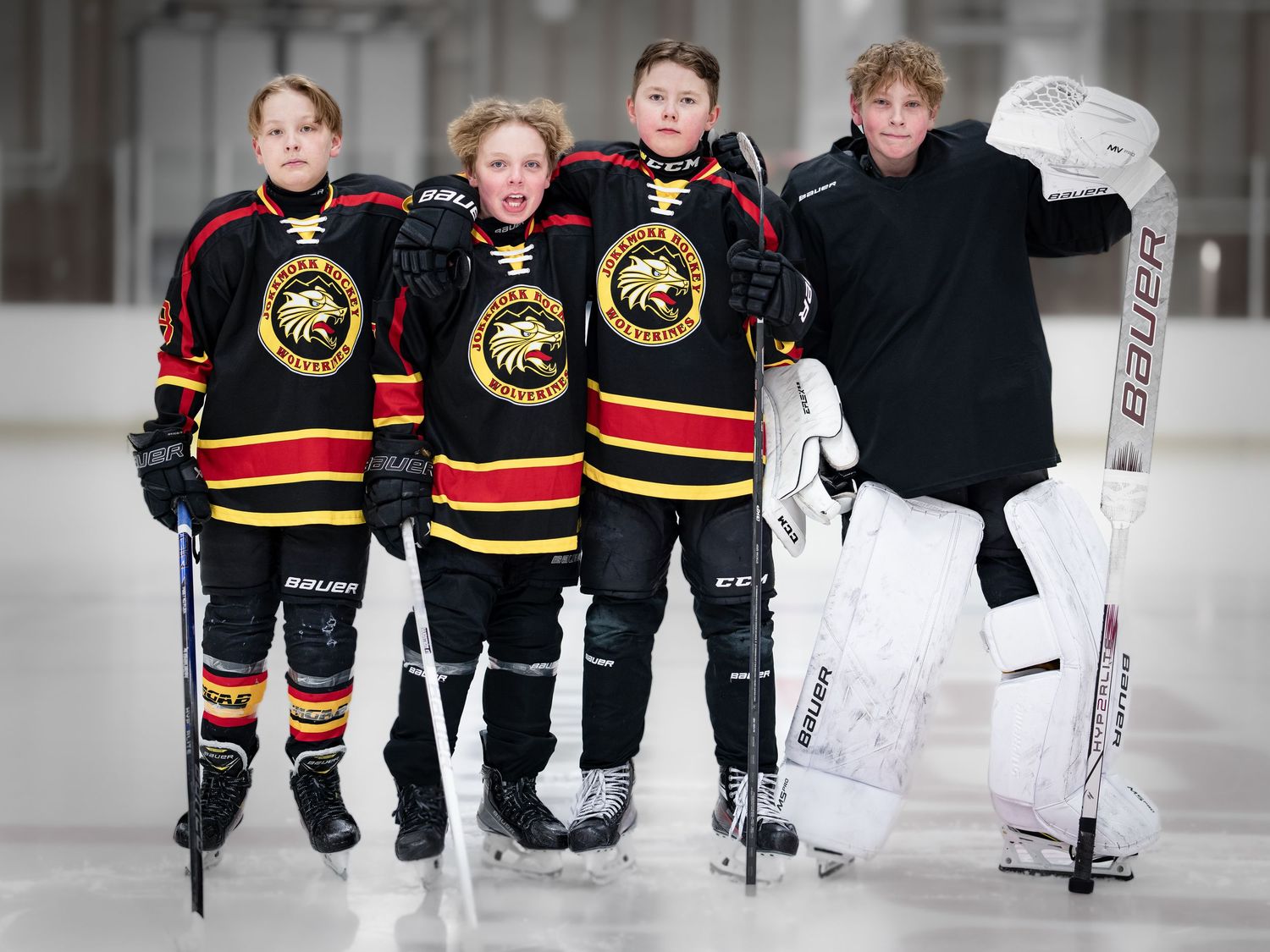 Fyra unga hockeyspelare i svarta och guldfärgade uniformer poserar tillsammans på isbanan.