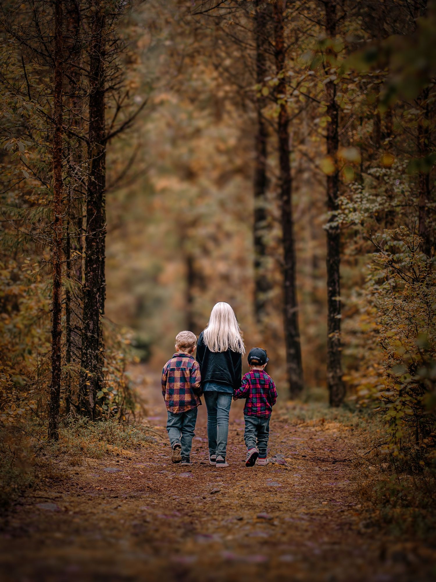 Three small figures walk together on an autumn forest path covered in fallen leaves.