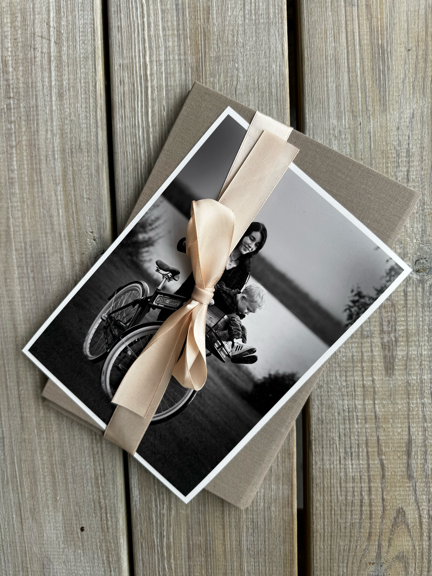 Old black and white photographs of a motorcycle rider tied together with a beige ribbon on weathered wooden planks.