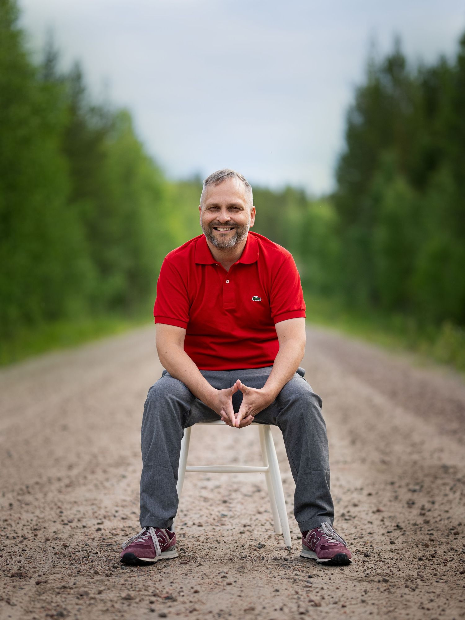 Someone sits in a white chair on a dirt road surrounded by green trees and natural scenery.