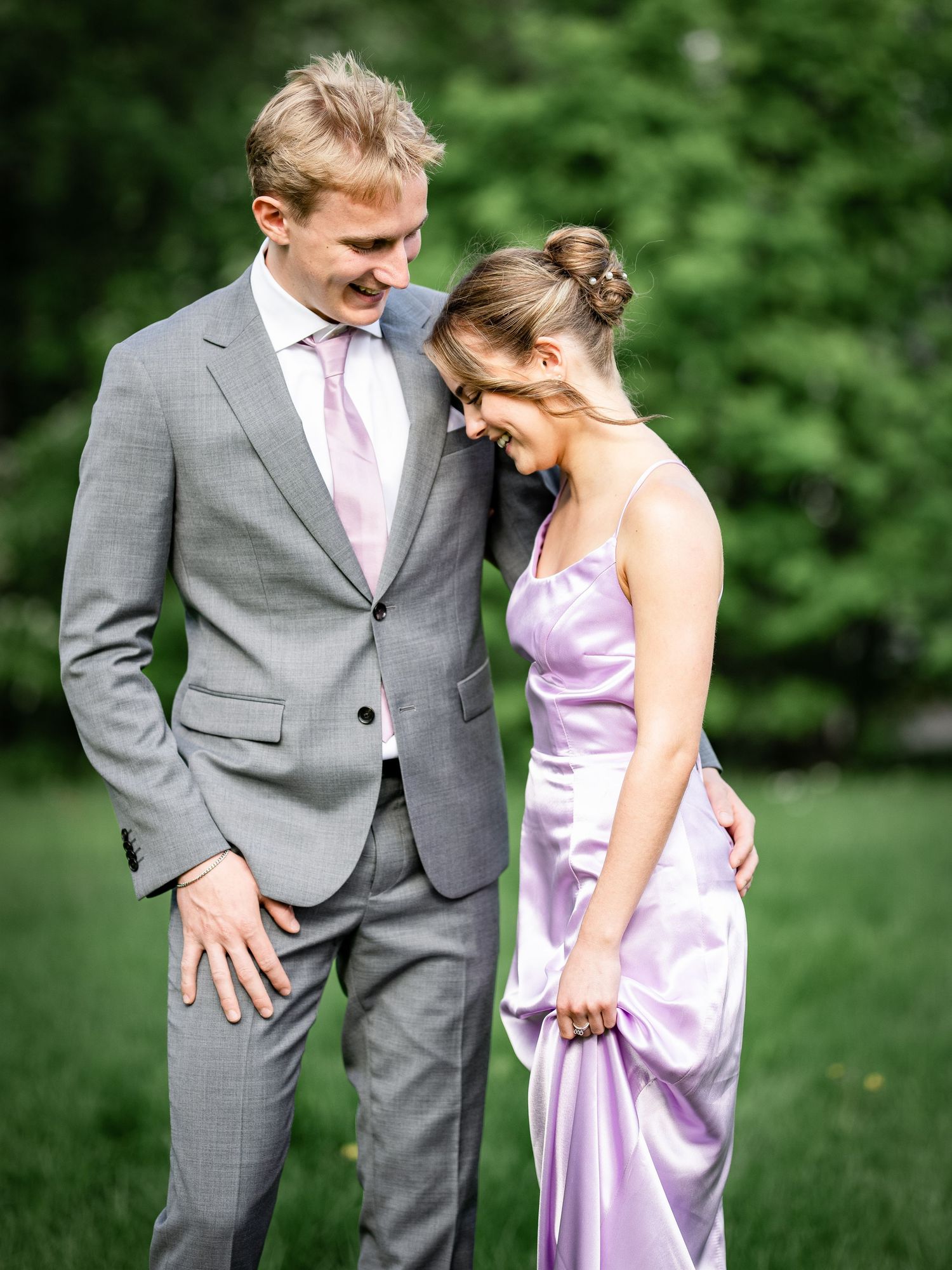A couple in formal attire share a tender moment outdoors in a garden setting.