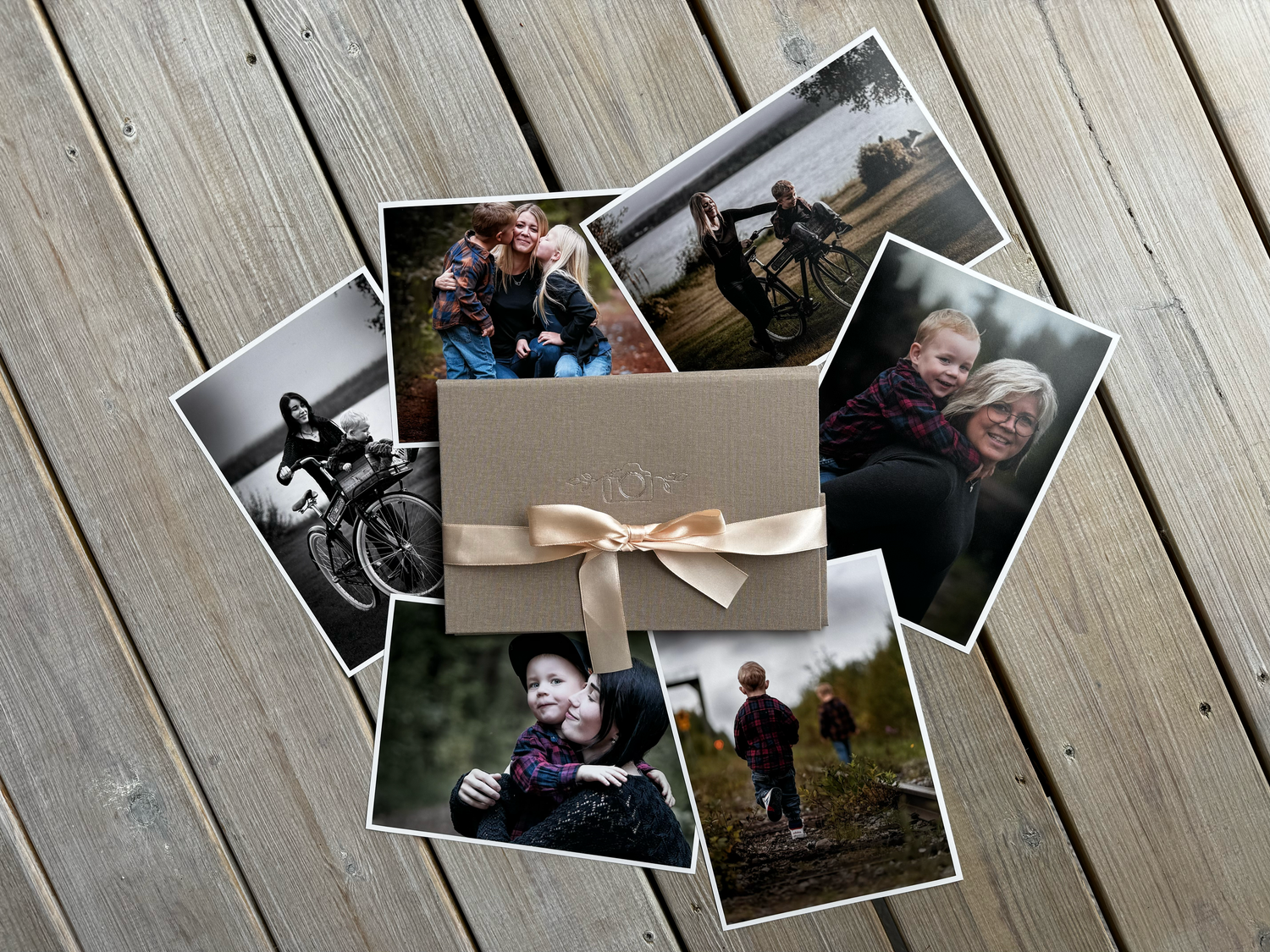 A collection of scattered photographs arranged in a circle with a beige bow-tied envelope in the center on wooden decking.