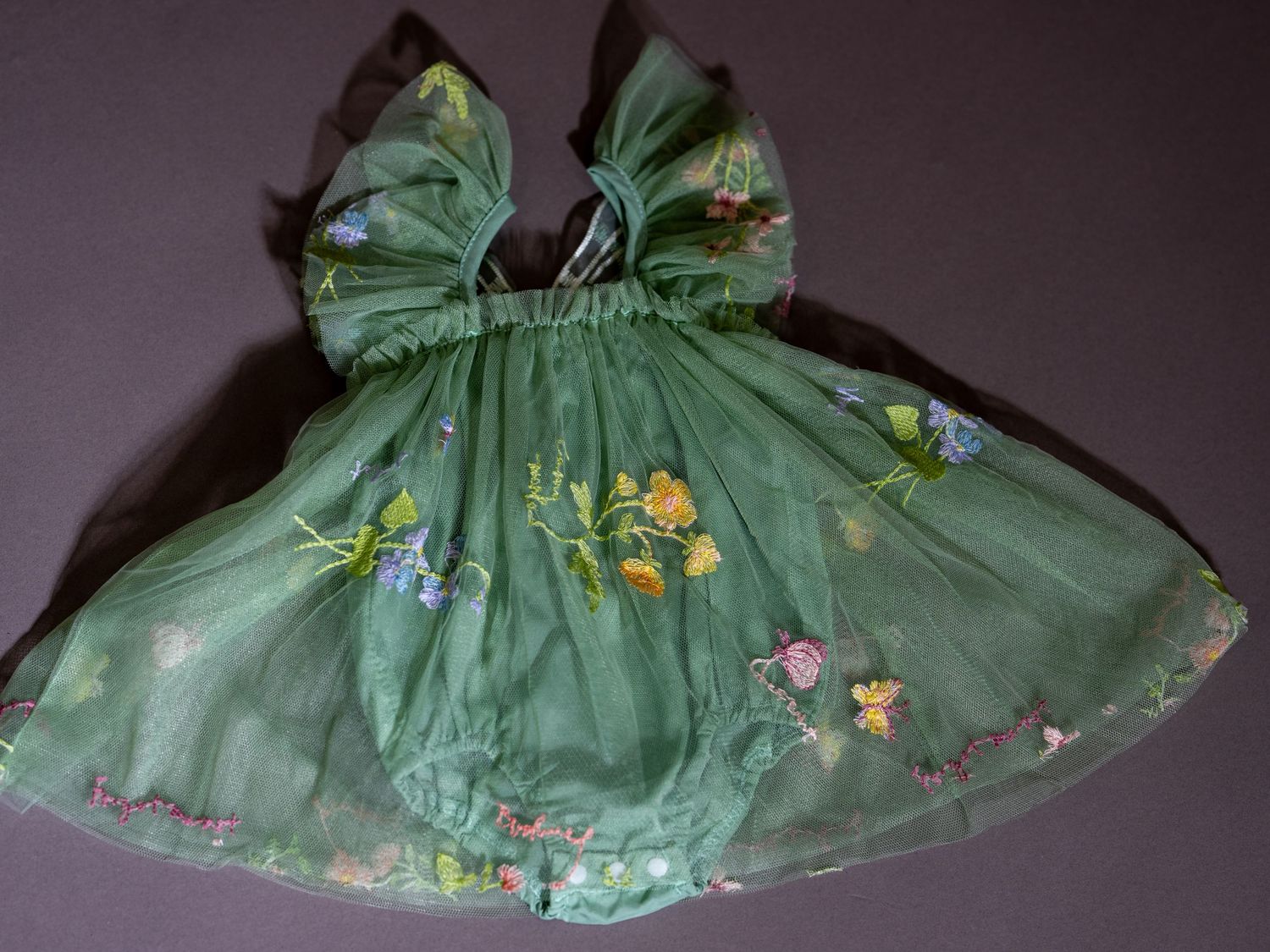 En grön vintage babyklänning med blombroderi visad från flera vinklar mot mörk bakgrund.