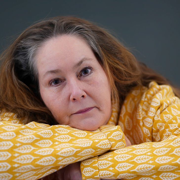Portrait against dark background with person resting on yellow patterned fabric.