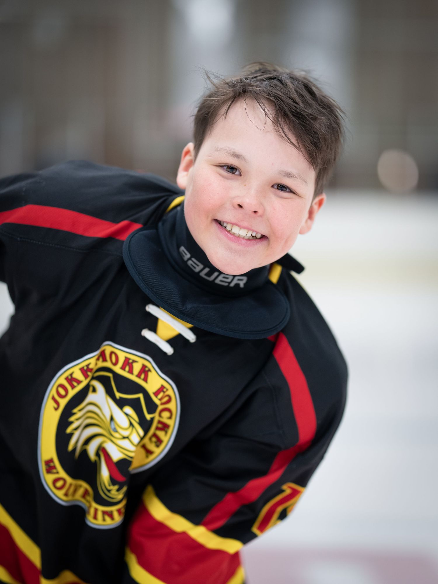 Ungdomshockeyspelare i svart och guld uniform ler på isbana.