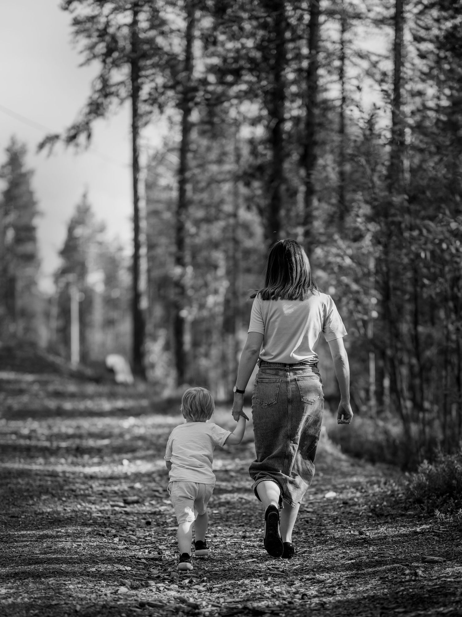 En svartvit bild av en förälder och ett barn som går hand i hand längs en skogsstig.