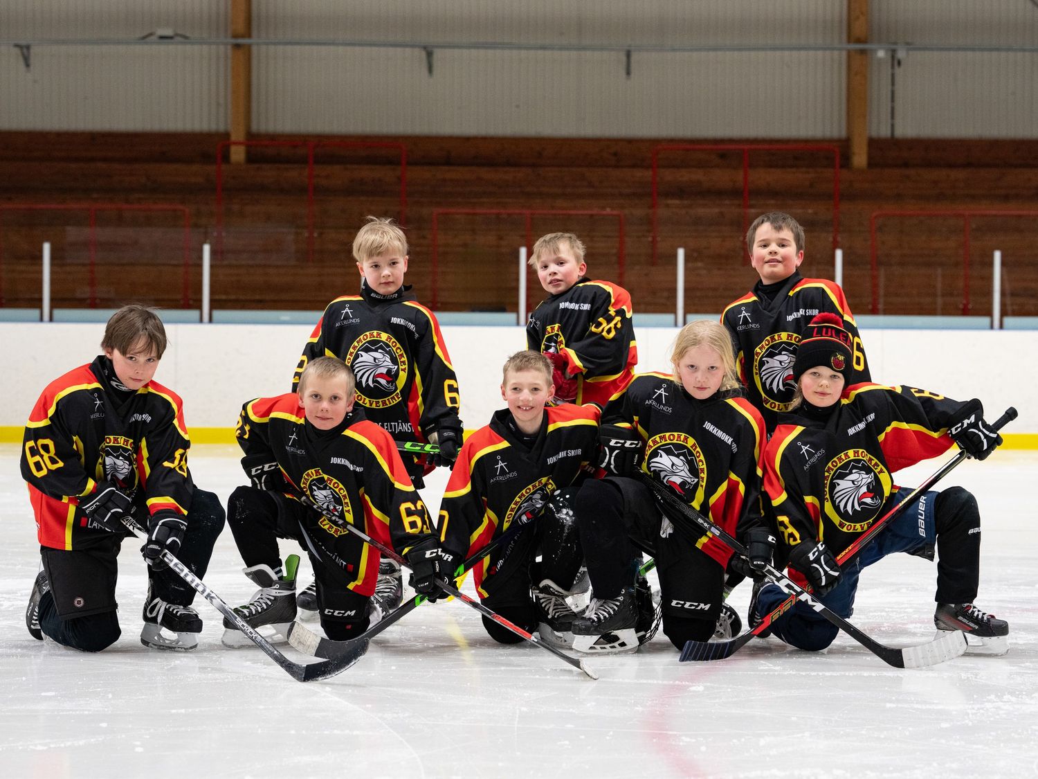 Ungdomshockeyspelare i svarta och guldiga tröjor poserar roliga för lagfoto på isen.