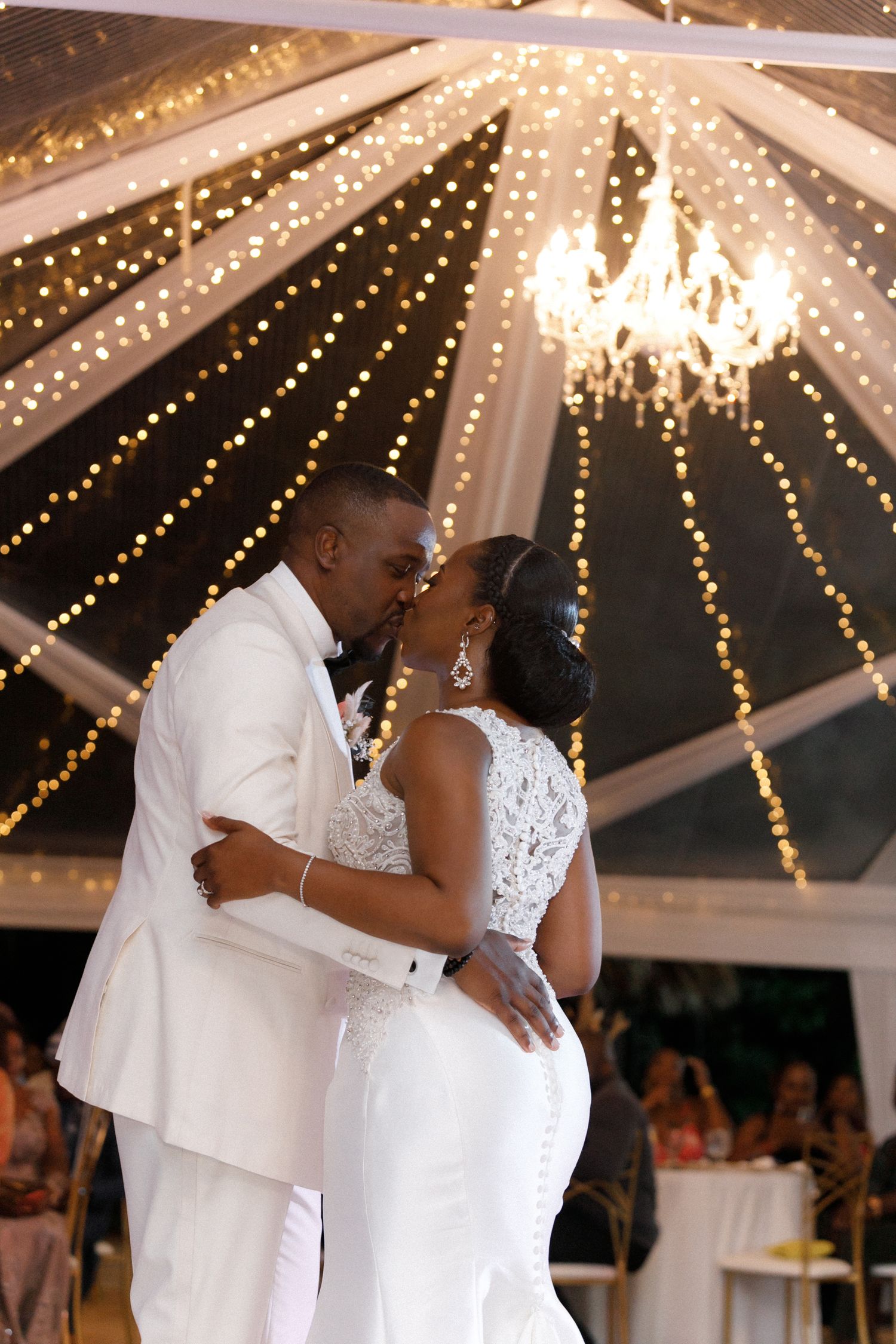 First dance under stunning chandelier and string lights at wedding reception.