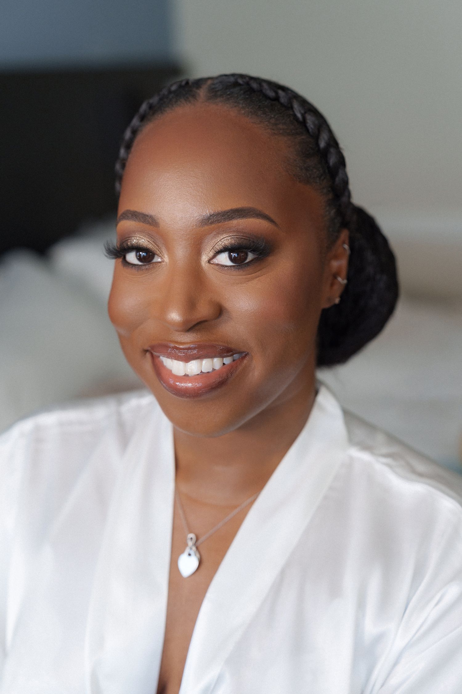 Woman in white robe with elegant braided updo and natural glam makeup.