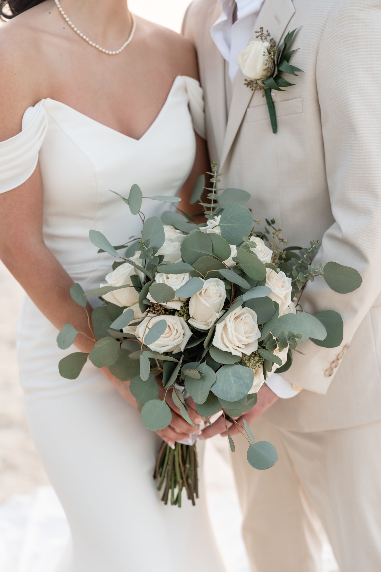 Wedding bouquet with white roses and eucalyptus leaves against ivory formal attire.