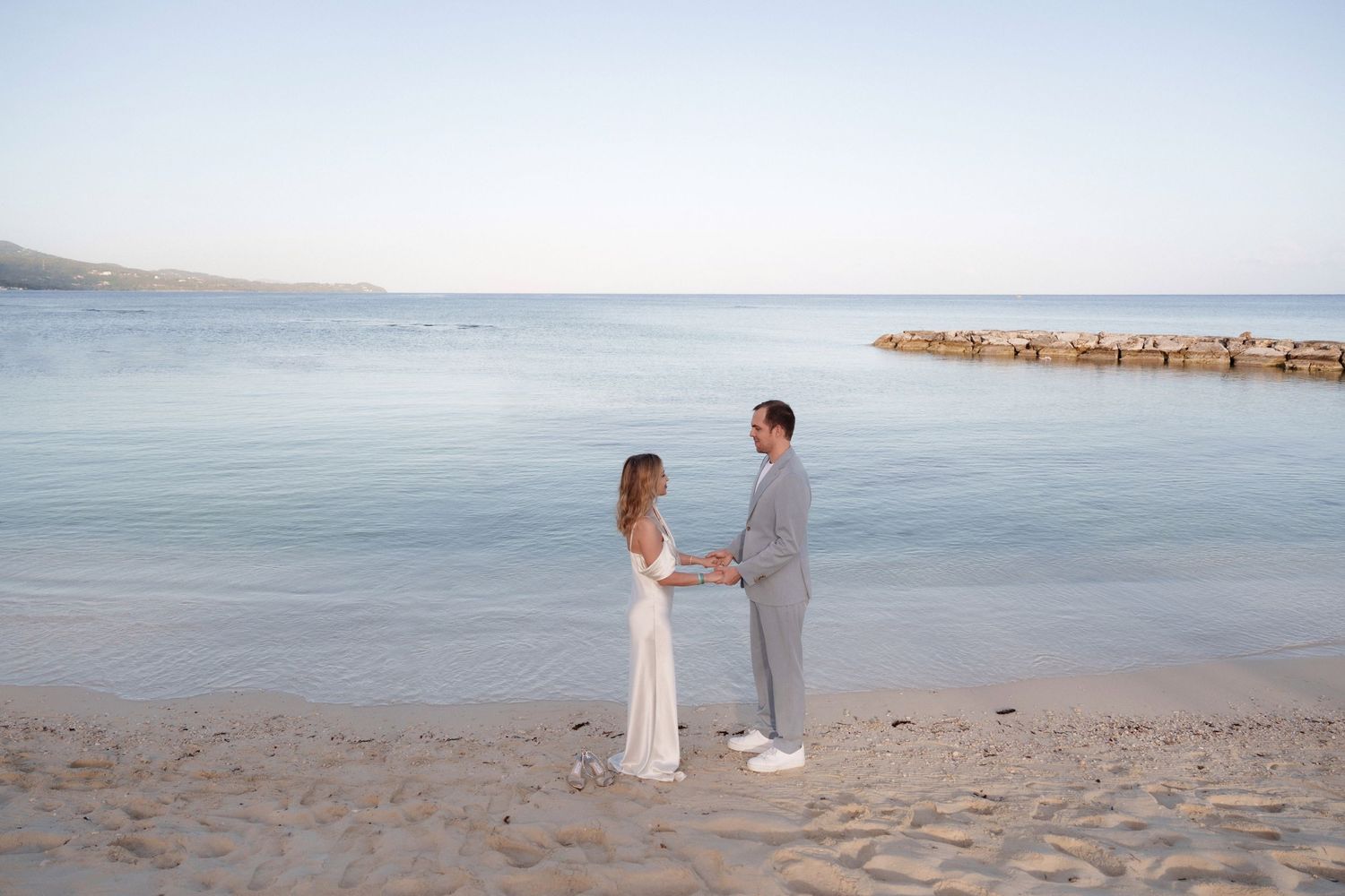 A couple in elegant attire sharing a moment on a sandy beach at dusk.