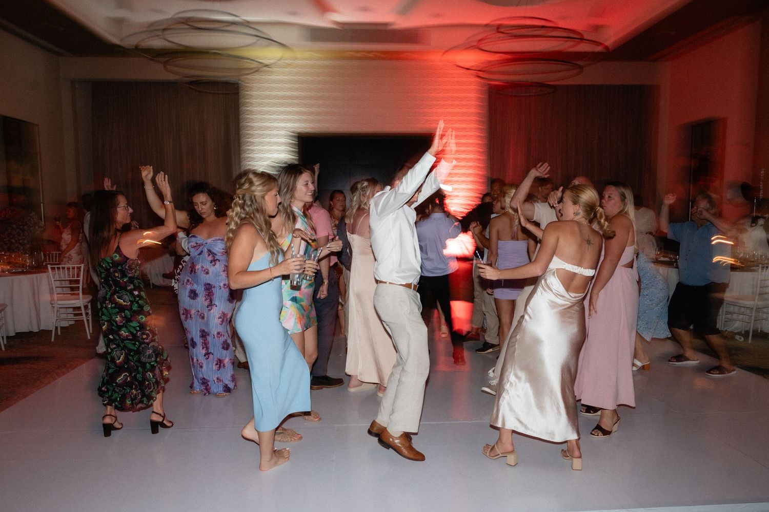 Wedding guests dancing on illuminated dance floor with red and white lighting.