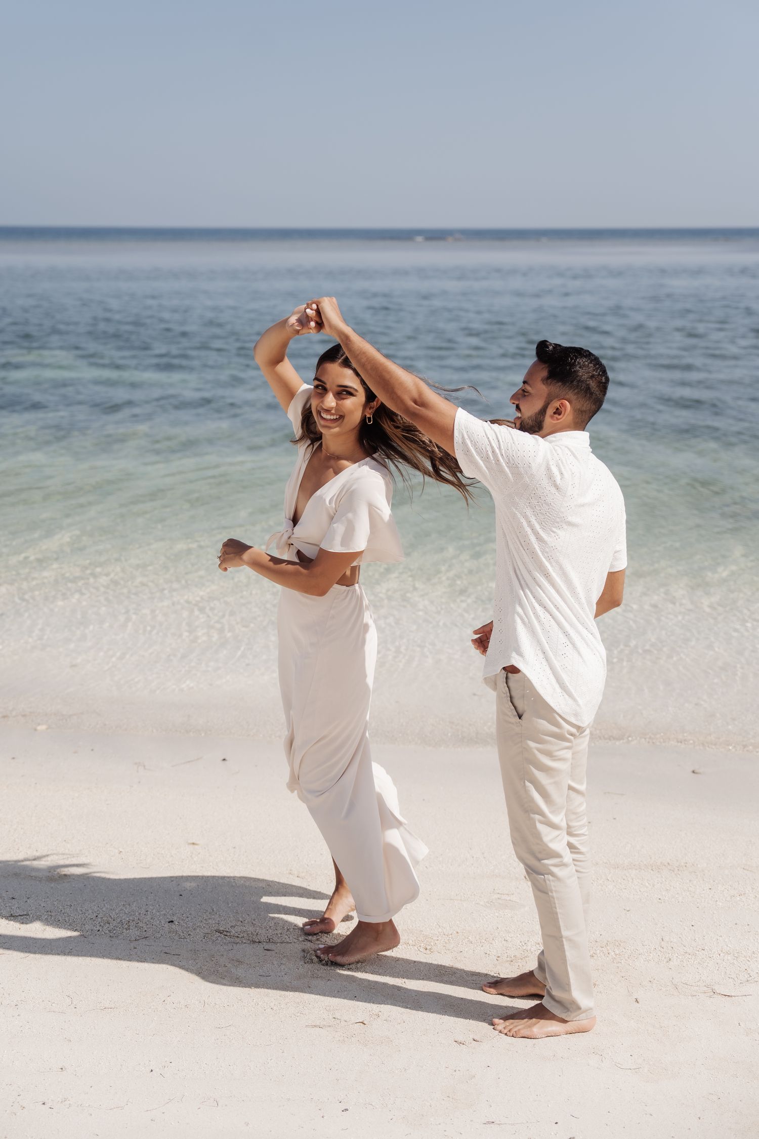A couple dancing together on a pristine white sand beach with turquoise waters in the background.