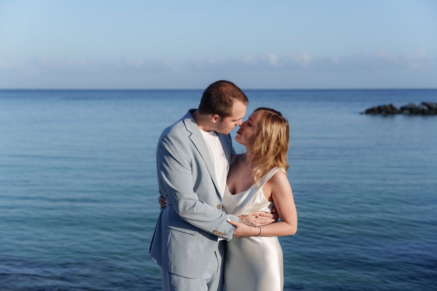 Intimate moment captured between newlyweds against serene ocean backdrop.