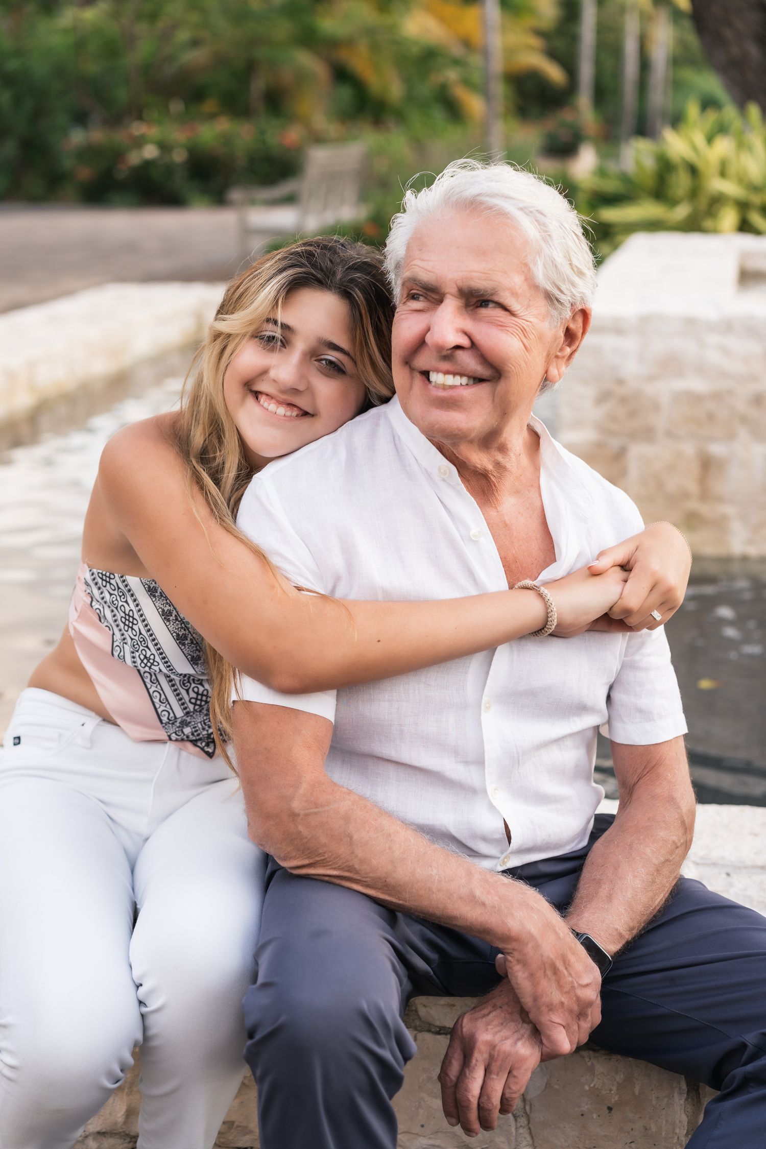 A heartwarming embrace captured outdoors with casual summer attire against a natural garden backdrop.