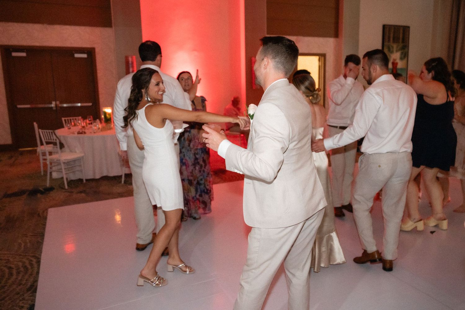Wedding guests dancing on a dance floor with pink and red lighting.