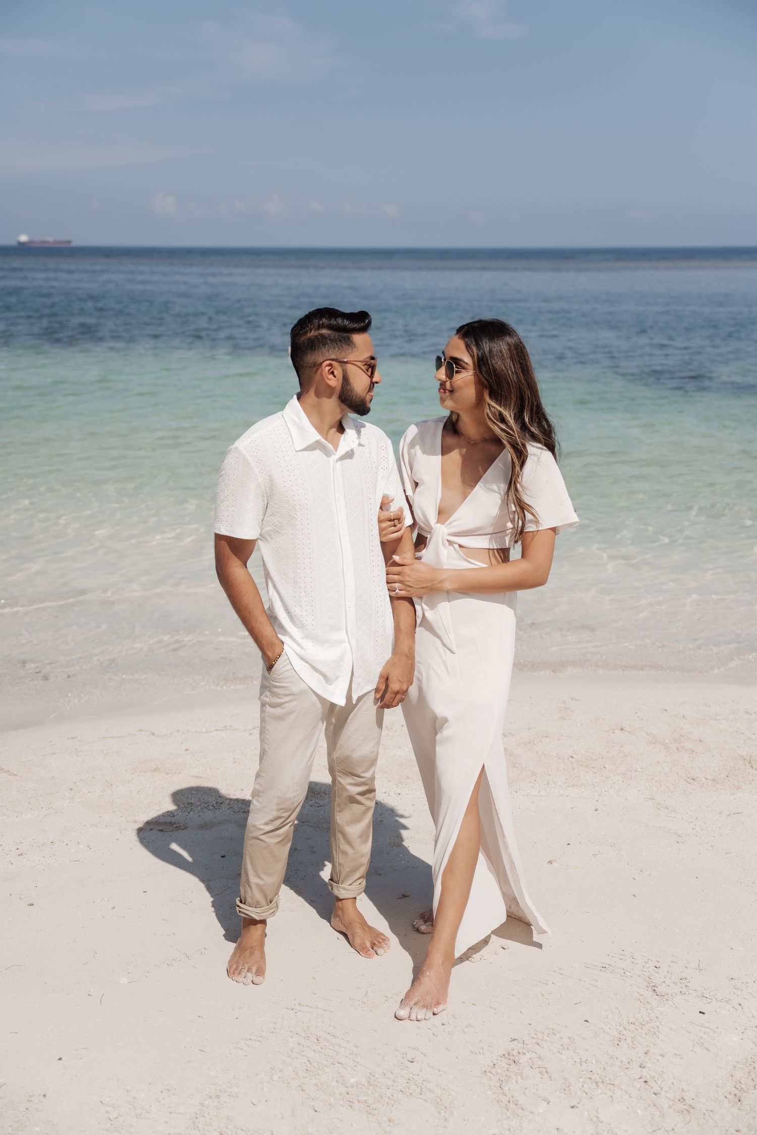 A couple in matching white outfits sharing a romantic moment on a secluded beach.