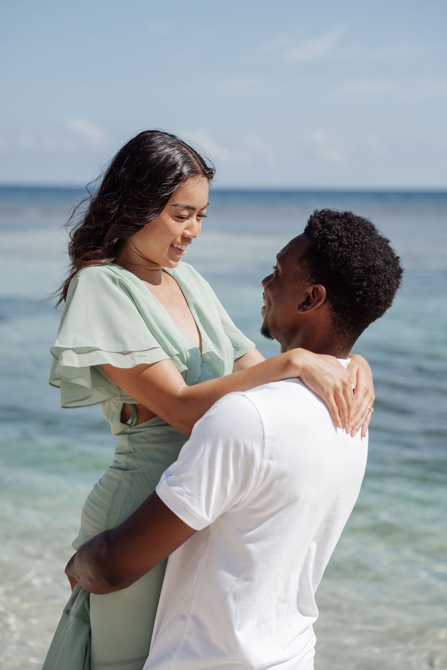 A couple shares a playful moment by the ocean, with gentle waves in the background.