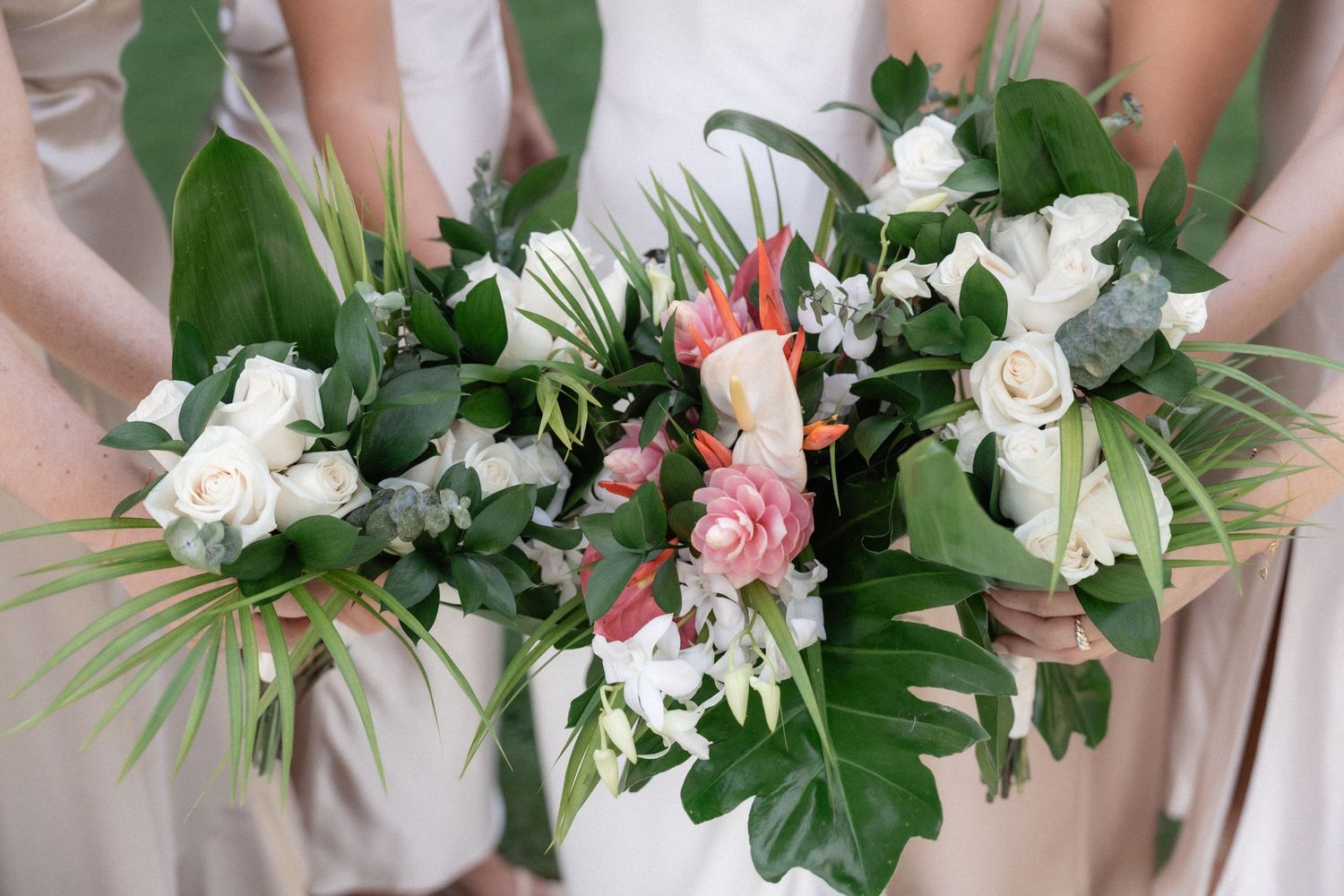 Elegant wedding bouquets featuring white roses, pink flowers, and tropical greenery.