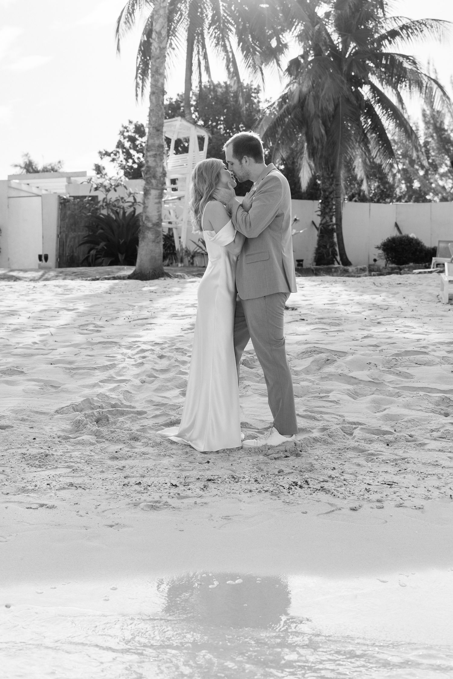 Black and white photo of couple in formal wear embracing near palm trees.