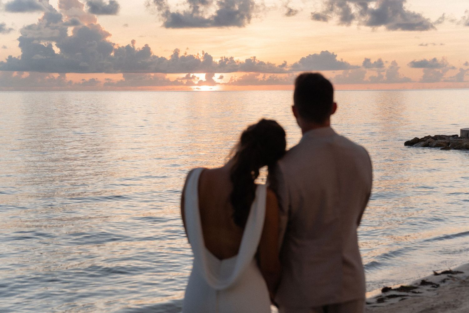 Couple watches sunset together on tropical beach in romantic silhouette.