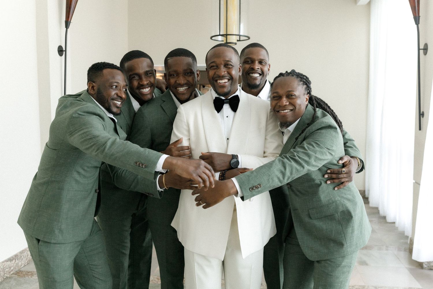 Wedding party joins together in celebratory group hug wearing coordinated formal attire.
